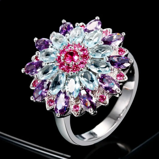 Bague en argent en forme de fleur, ornée de pierres précieuses roses, violettes et bleues claires disposées en couches.