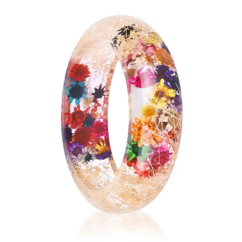 Bracelet en résine transparente contenant des fleurs séchées colorées et des accents métalliques.