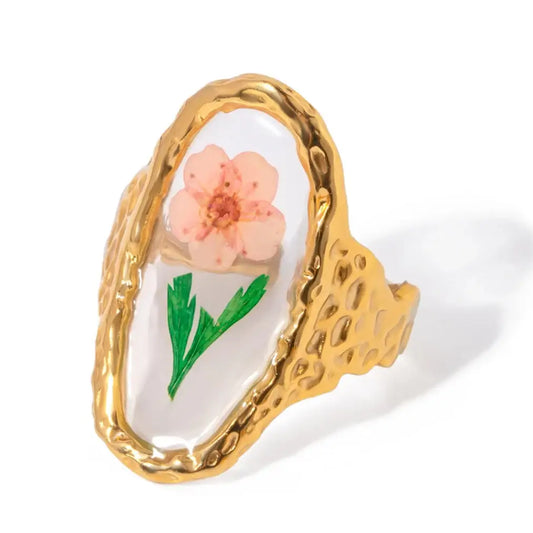 Bague en or présentant un motif de fleur rose sous verre ou résine transparente.