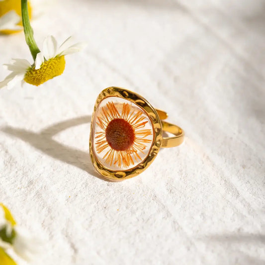 Bague en or ornée d’une fleur de marguerite conservée dans une résine transparente.