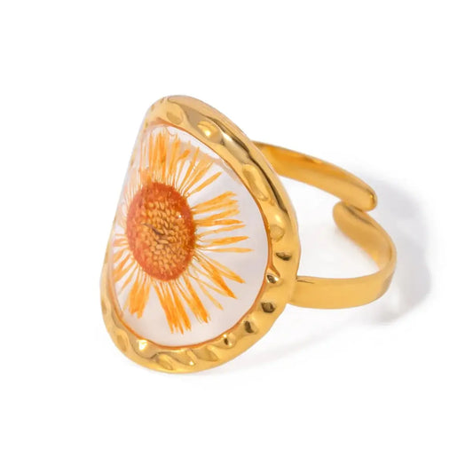 Bague en plaqué or ornée d’une fleur de marguerite conservée dans une résine transparente.