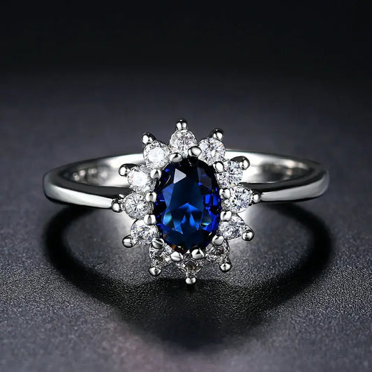 Bague en argent ornée d’un saphir bleu ovale entouré de diamants blancs dans un halo floral.