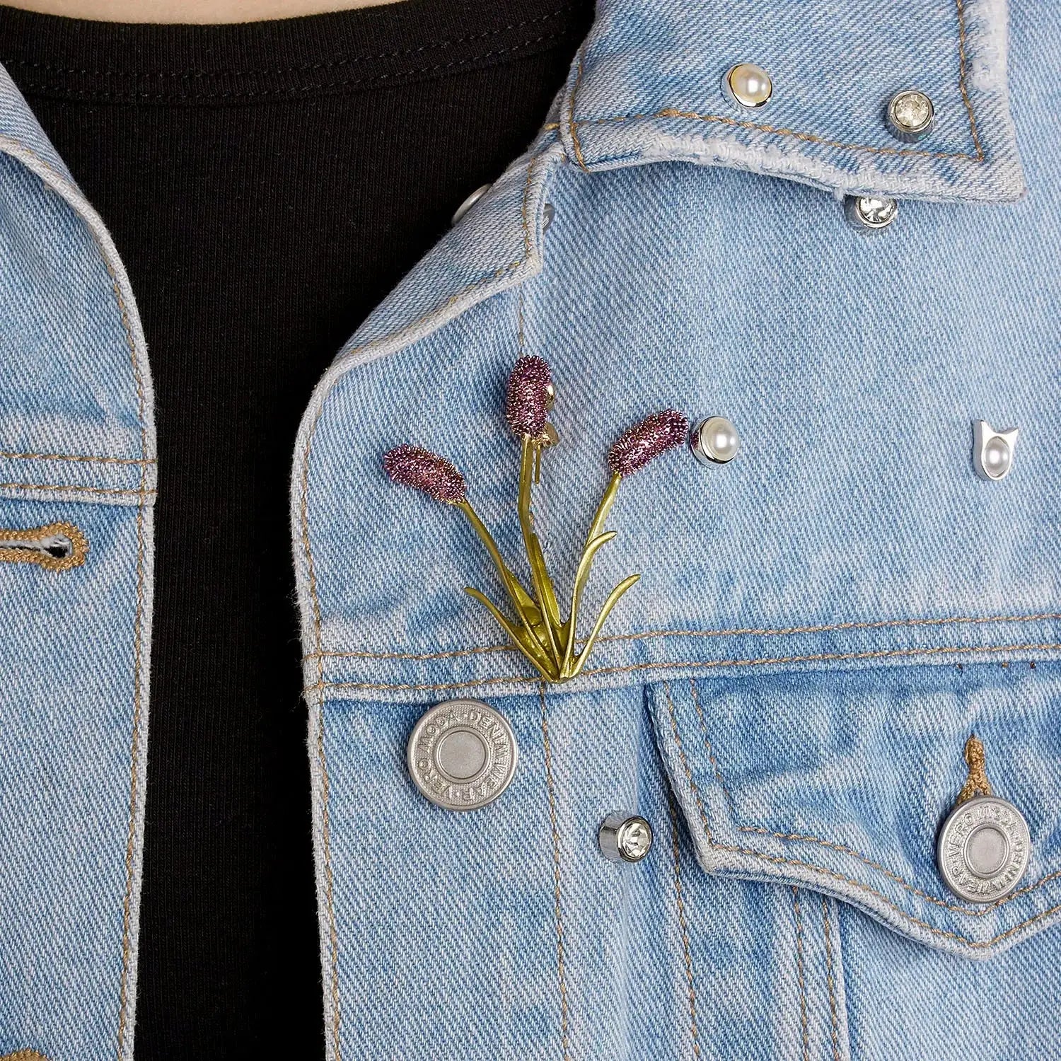 Délicate broche en forme de fleur violette épinglée sur une veste en jean clair.